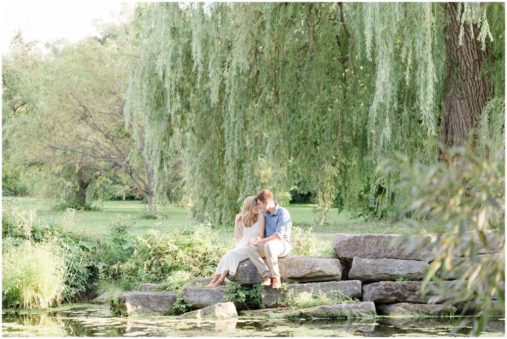 dominion arboretum engagement couple sitting on rocks by river in front of willow tree