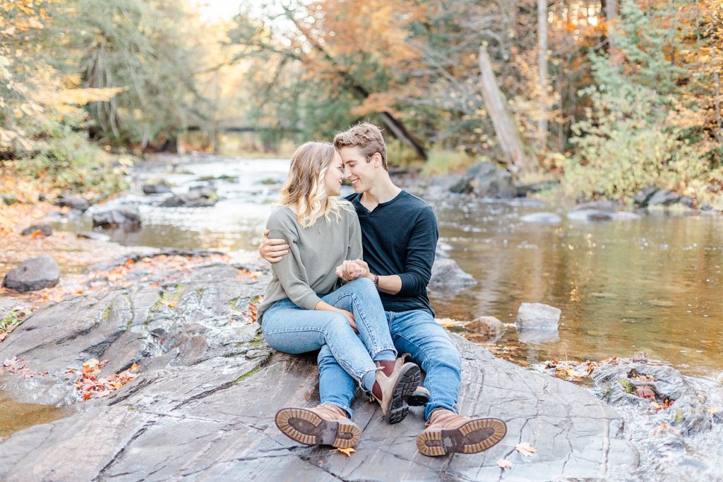 couple sitting on rock in the middle of water during fall infused engagement session