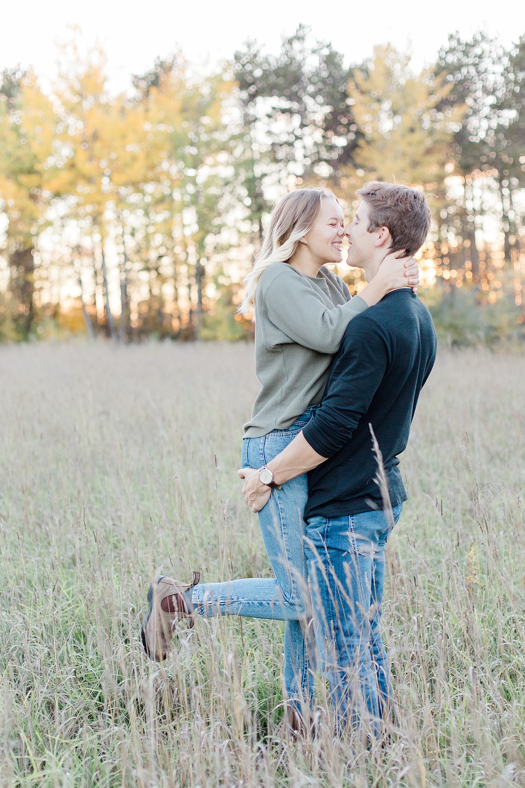 guy picking up girl in the middle of a field during sunset in the fall