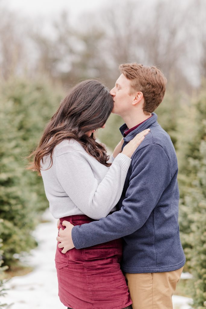 guy giving his fiance a forehead kiss at the christas tree farm