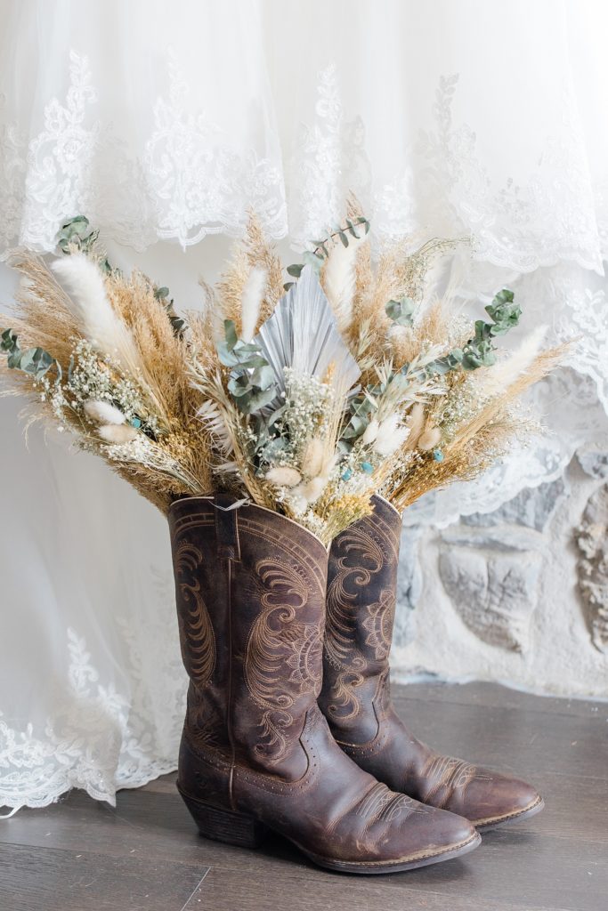 dried floral bridal bouquet in cawgirl boots with wedding dress as background 