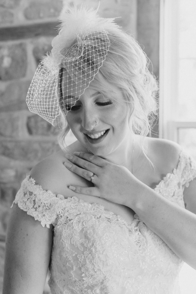 black and white image of bride wearing a bird cage veil, looking down over her shoulder and showcasing her engagement ring
