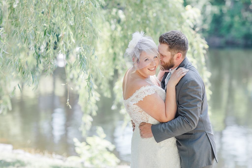 bride is smiling towards the camera as the groom is about to kiss her cheek during their formal photos