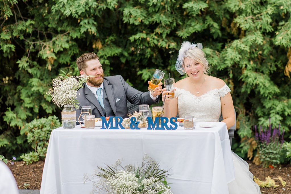 bride and groom raising a glass for a toast as they are sitting at the Mr. and Mrs. table during their reception at the carleton golf and yacht club