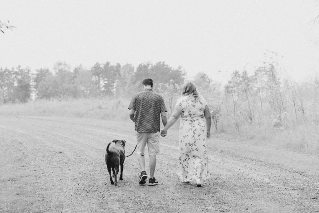 couple walking away with their dog while  holding hands  during Almonte engagement session with Brittany Navin Photography