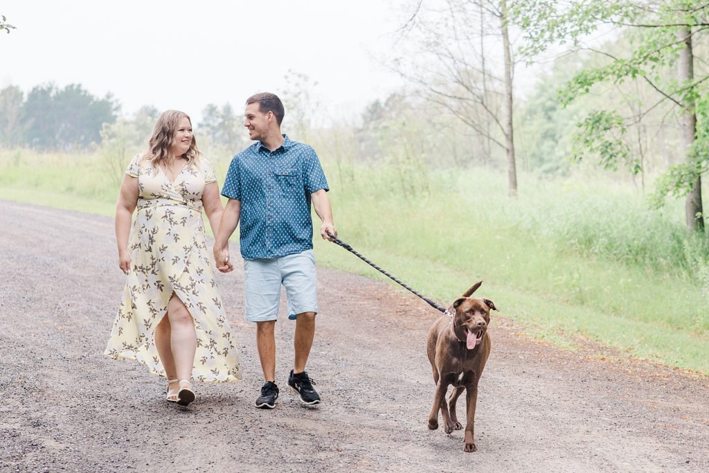 couple walking their dog while holding hands at rainy summer Mill of Kintail Engagement session with Brittany Navin Photography in Almonte, ON