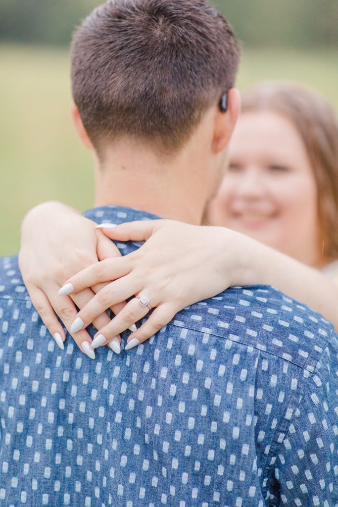 close up of engagement ring as her hands are draped around his neck at rainy summer Mill of Kintail Engagement session with Brittany Navin Photography in Almonte, ON