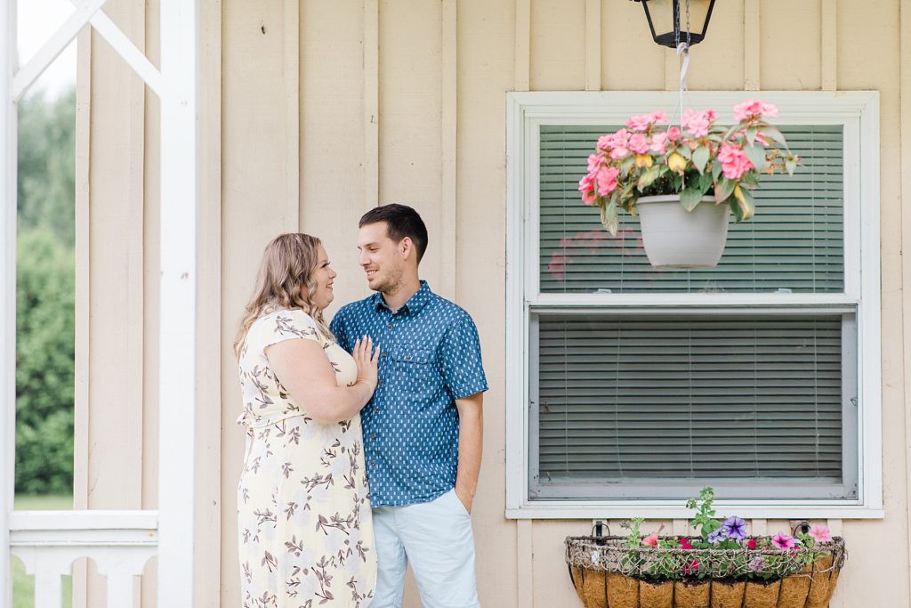 couple pulled in close to each other under porch at rainy summer Mill of Kintail Engagement session with Brittany Navin Photography in Almonte, ON