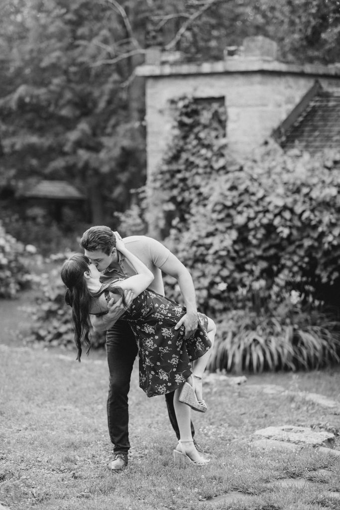 he is dipping her down for a kiss in front of stone building covered in vines at engagement in Almonte, ON, at the Mill of Kintail with Brittany Navin Photography