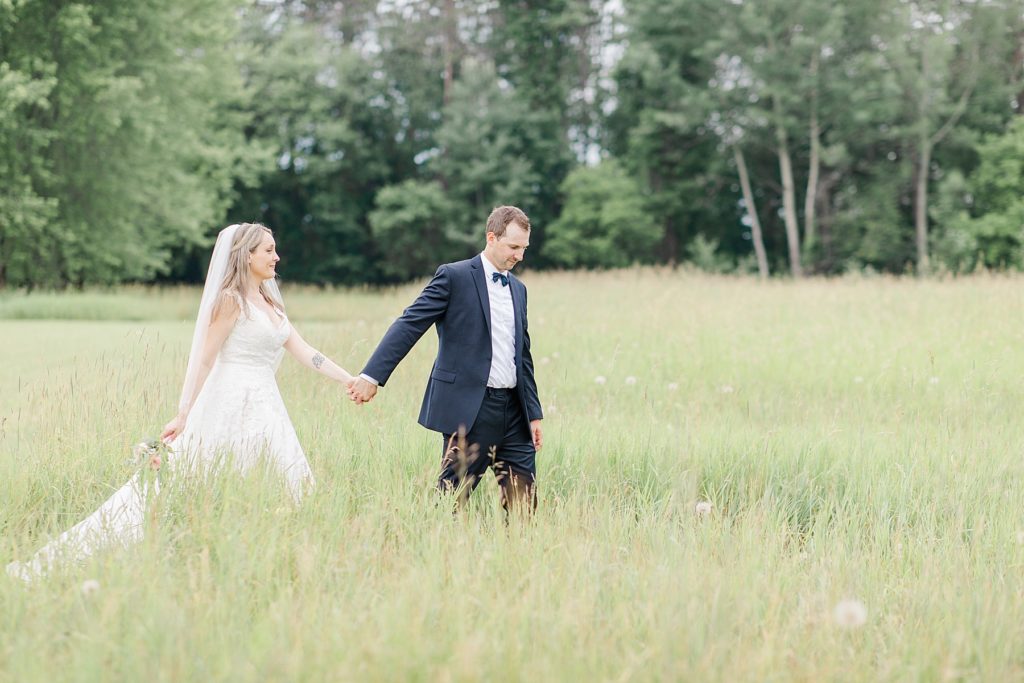 bride and groom walking through long grass field at Mill of Kintail Wedding with Brittany Navin Photography in Almonte, Ontario