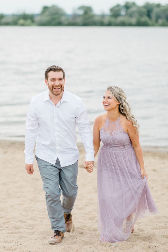 fiances laughing with each other as they walk holding hands during their ottawa beach engagement session