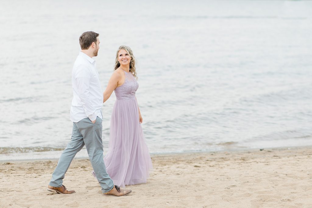 bride to be leading the way as she holds groom to be's hand and walks along the water at otttawa beach engagement session