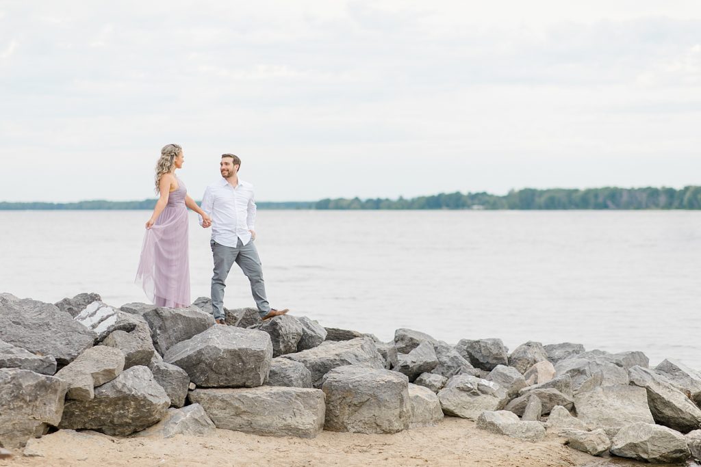 fiance's walking along big rocks that are on the side of the petire island beach in ottawa