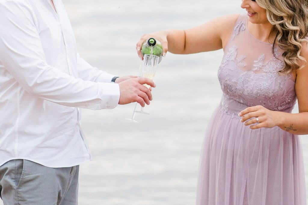 she is pouring her fiance a glass of champagne during Petrie Island Beach Engagement session