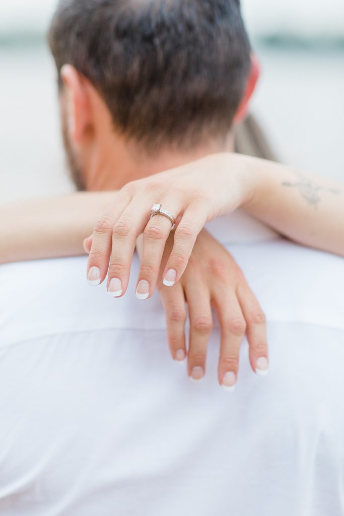 close up of engagement ring while her hands are draped around his neck during Petrie Island Beach Engagement session