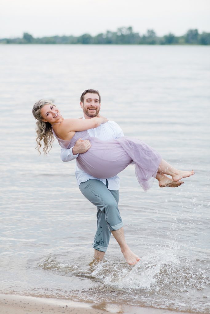 groom to be carrying his fiance through the water during ottawa beach engagement session