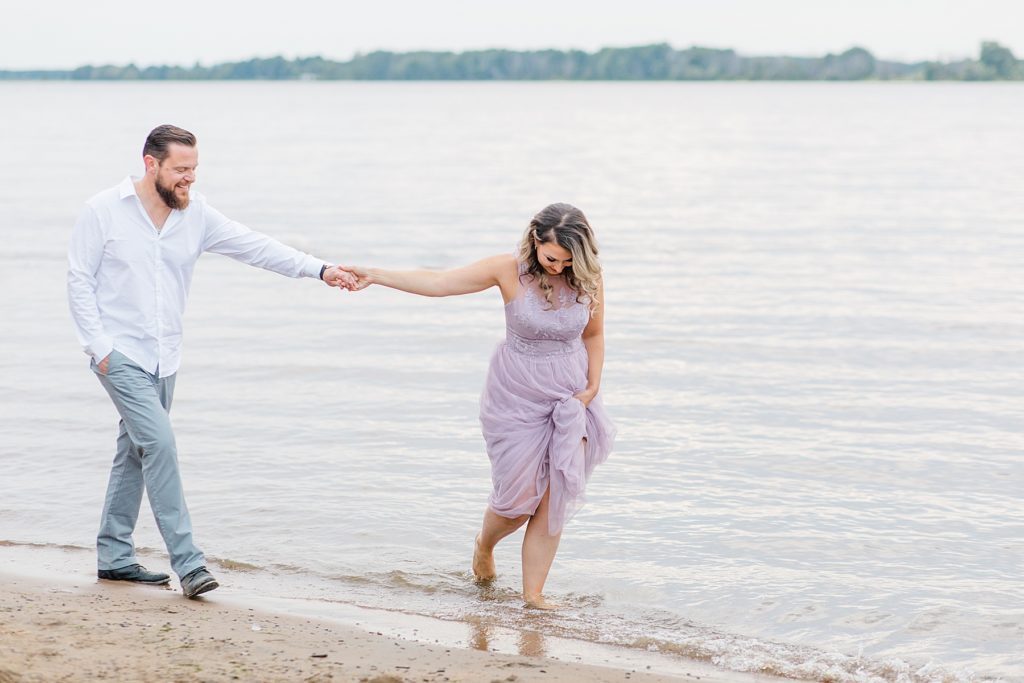 couple walking along the water all dressed up for their Petrie Island Beach Engagement session
