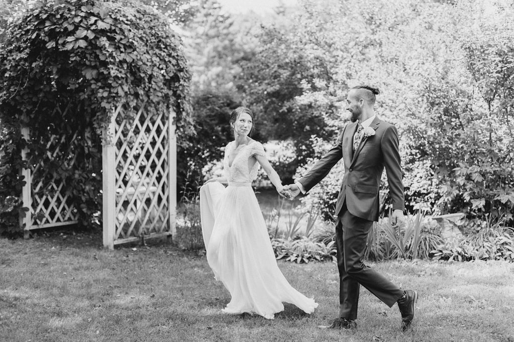 bride and groom walking by the church garden At The Schoolhouse wedding in munster ontario photographed by Brittany Navin Photography