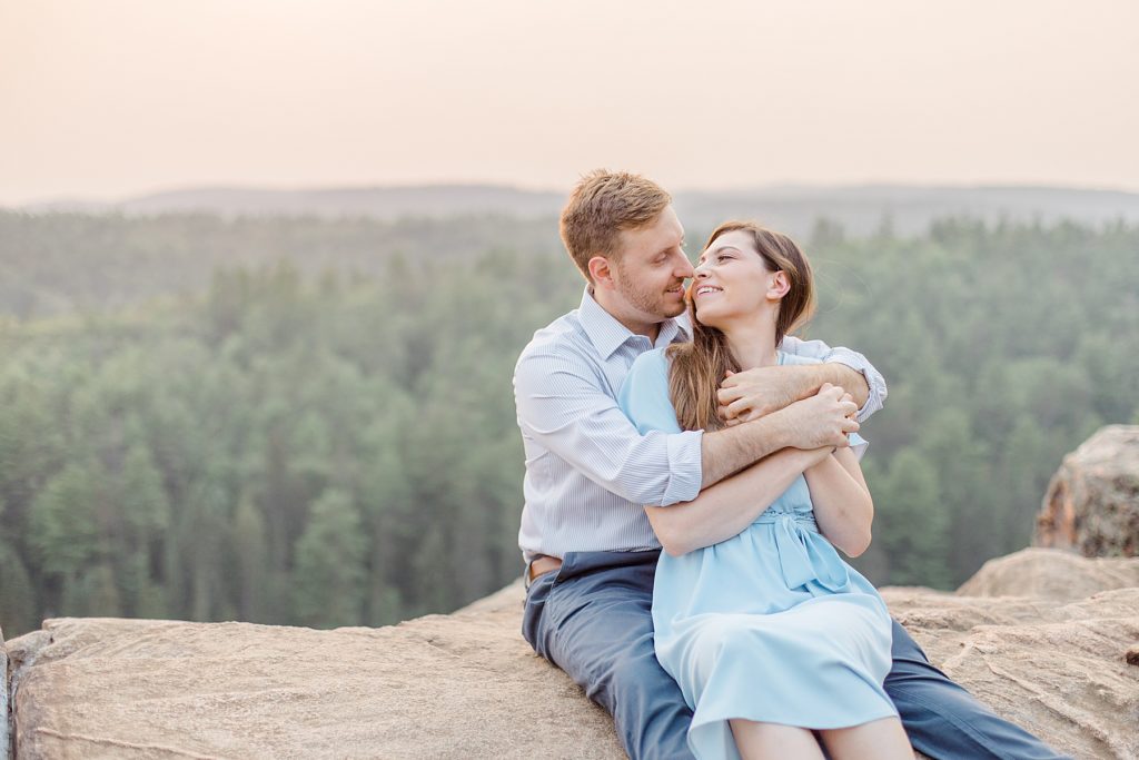 couple sitting together with pink sunset behind them at Eagle's Nest Engagement in Calabogie, Ontario with Brittany Navin Photography