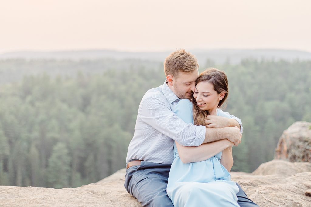 he is wrapping her up with pink sky behind them at Eagle's Nest Lookout Engagement in Calabogie, Ontario with Brittany Navin Photography