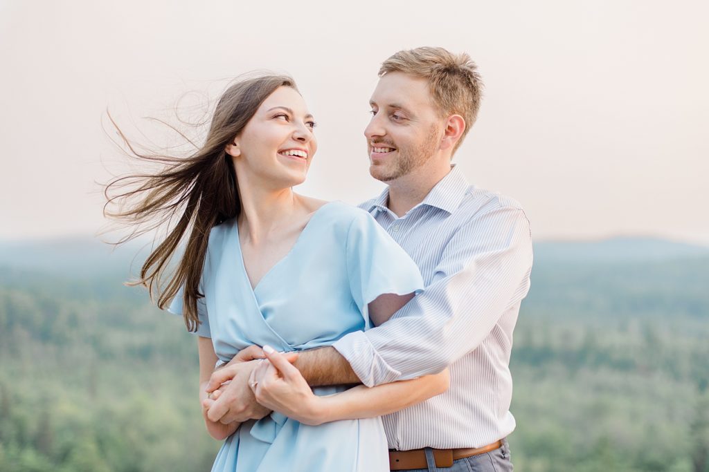 couple laughing as wind causes her hair to fly at Eagle's Nest Lookout Engagement in Calabogie, Ontario with Brittany Navin Photography