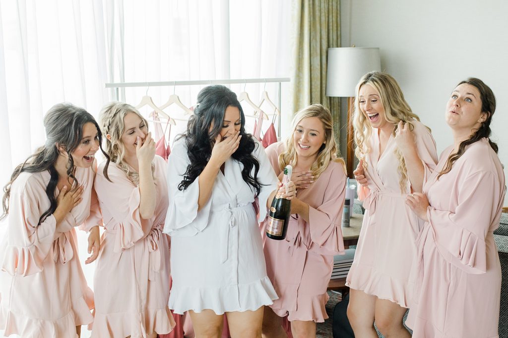 bride and bridal party pop champagne in matching pink robes at Adelina Barn Wedding Photographed By Brittany Navin Photography