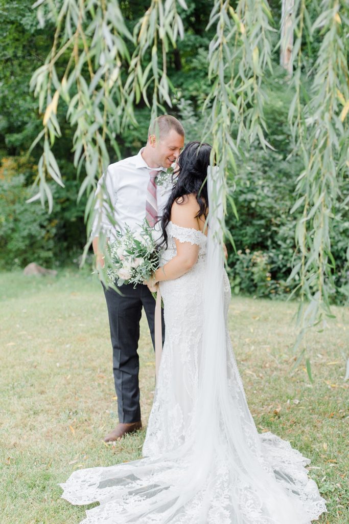 bride and groom having a moment photographed through the willow tree at Adelina Barn Wedding Photographed By Brittany Navin Photography