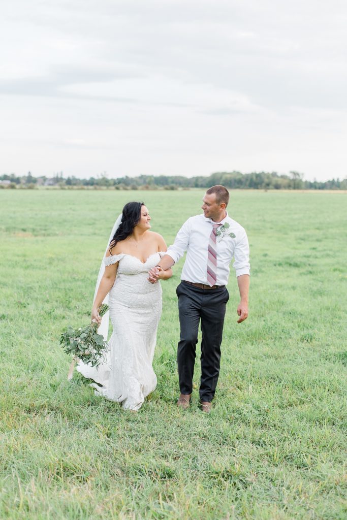 husband and wife walking through field at Adelina Barn Wedding Photographed By Brittany Navin Photography
