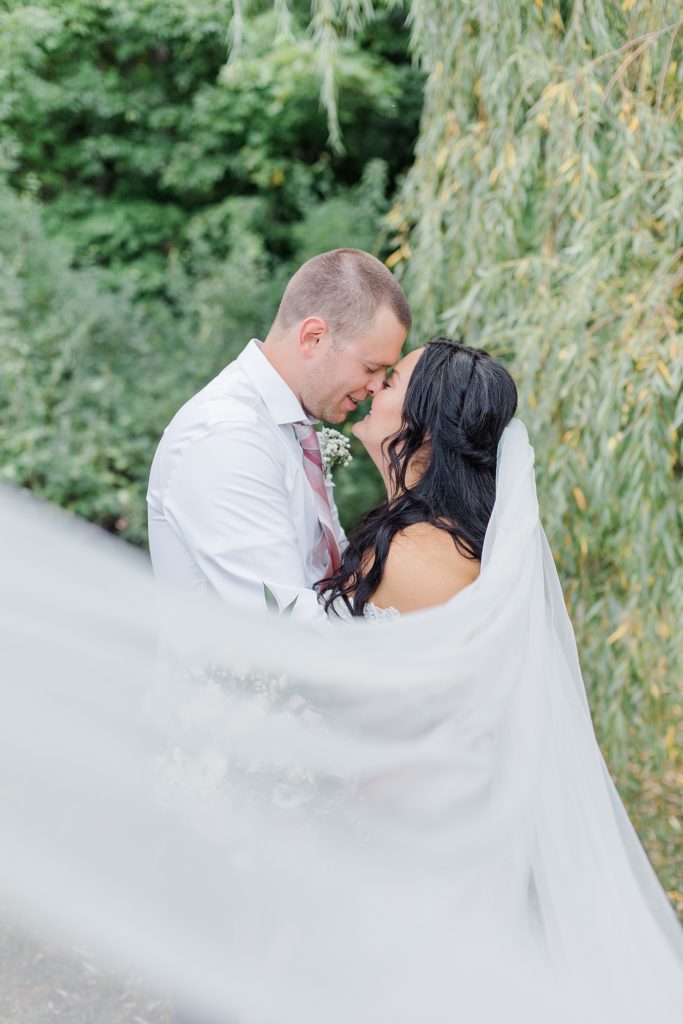 veil in foreground og husband and wife kissing at Adelina Barn Wedding Photographed By Brittany Navin Photography