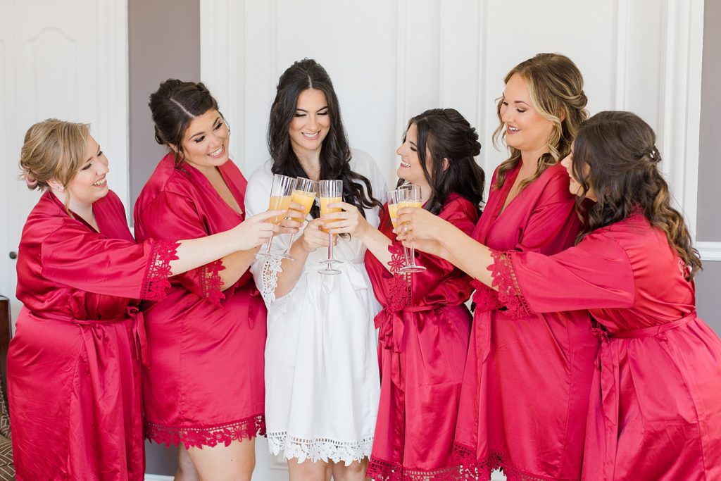 bride and bridesmaids in matching red robes cheersing their champagne at Grand Hotel in Carleton Place Photographed by Brittany Navin Photography