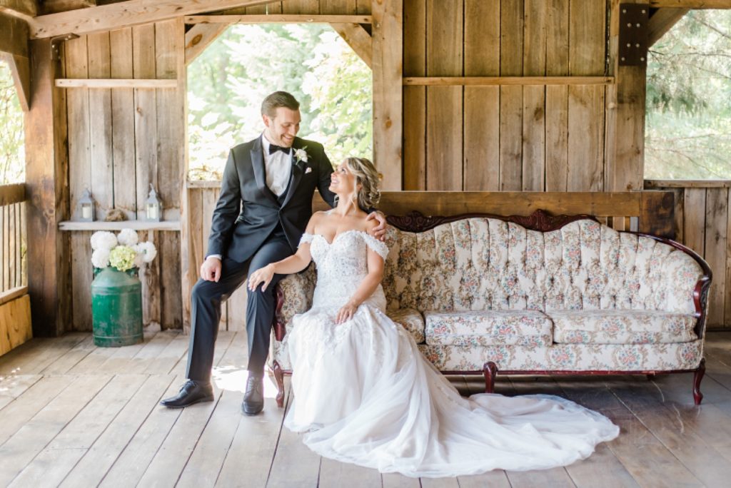 bride and groom in rustic barn on classy couch at bean town ranch double wedding photographed by Brittany Navin Photography