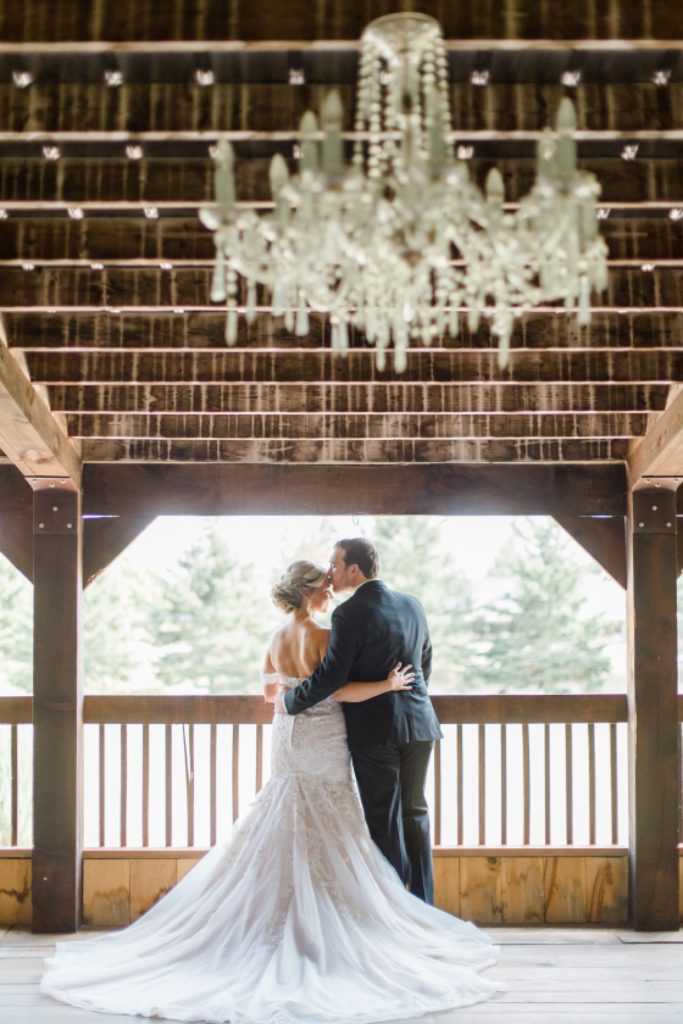 bride and groom standing at balcony under chandelier at bean town ranch double wedding photographed by Brittany Navin Photography