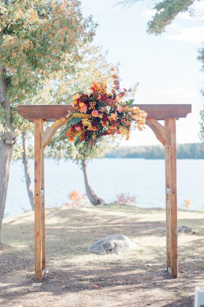 wooden wedding arch with fall florals at Calabogie Peaks wedding photographed by Brittany Navin Photography