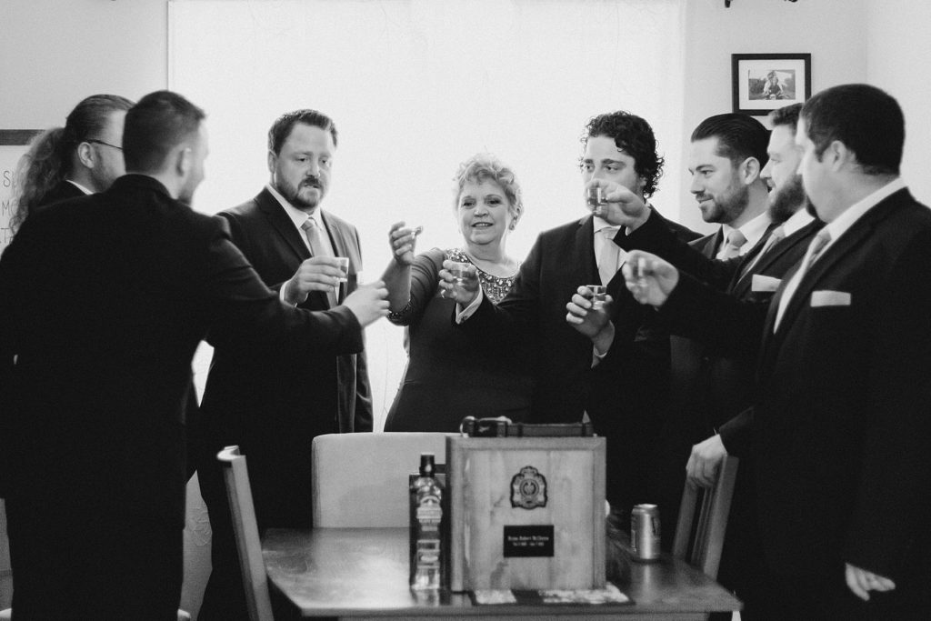 groom, grooms mom, and groomsmen taking a shot as tribute to grooms father as they get ready for temples country winter wedding photographed by Brittany Navin Photography