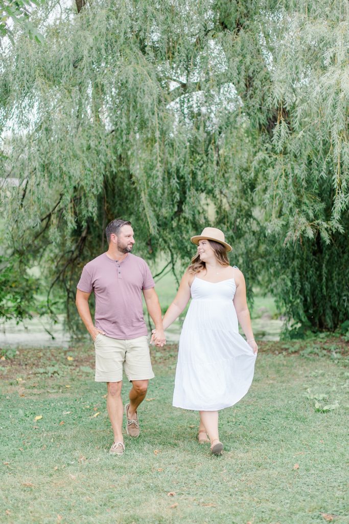 couple walking and looking at each other with willow tree behind them at dominion arboretum engagement session phtoographed by Brittany Navin Photography