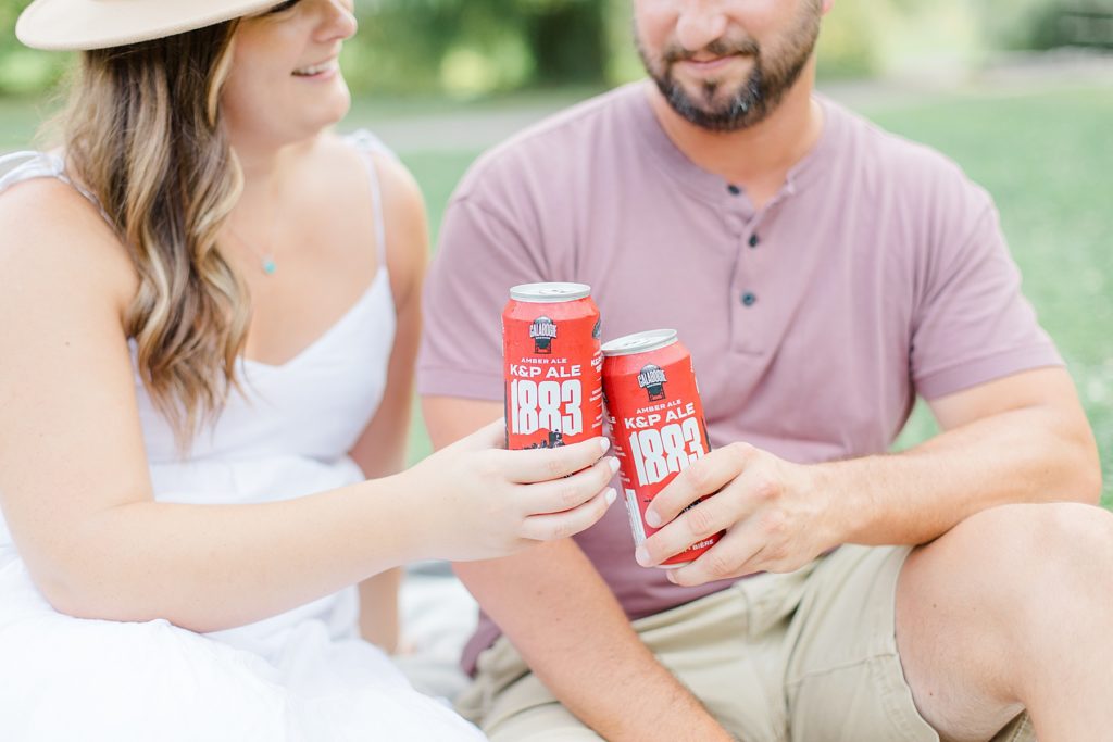 couple cheers their beer at picnic at dominion arboretum engagement session phtoographed by Brittany Navin Photography