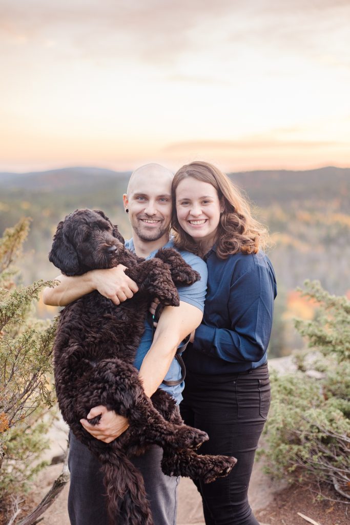 couple holding their pup while at the top of cliff during sunset at eagle's nest fall engagement photographed by Brittany Navin Photography