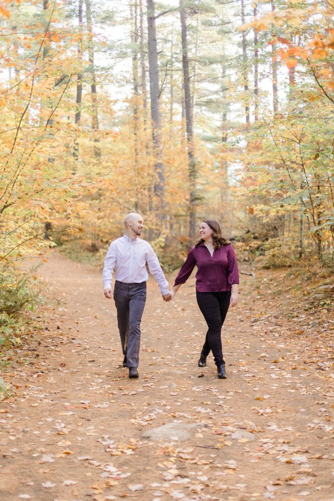couple walking through trail full of leaves at eagle's nest fall engagement photographed by Brittany Navin Photography
