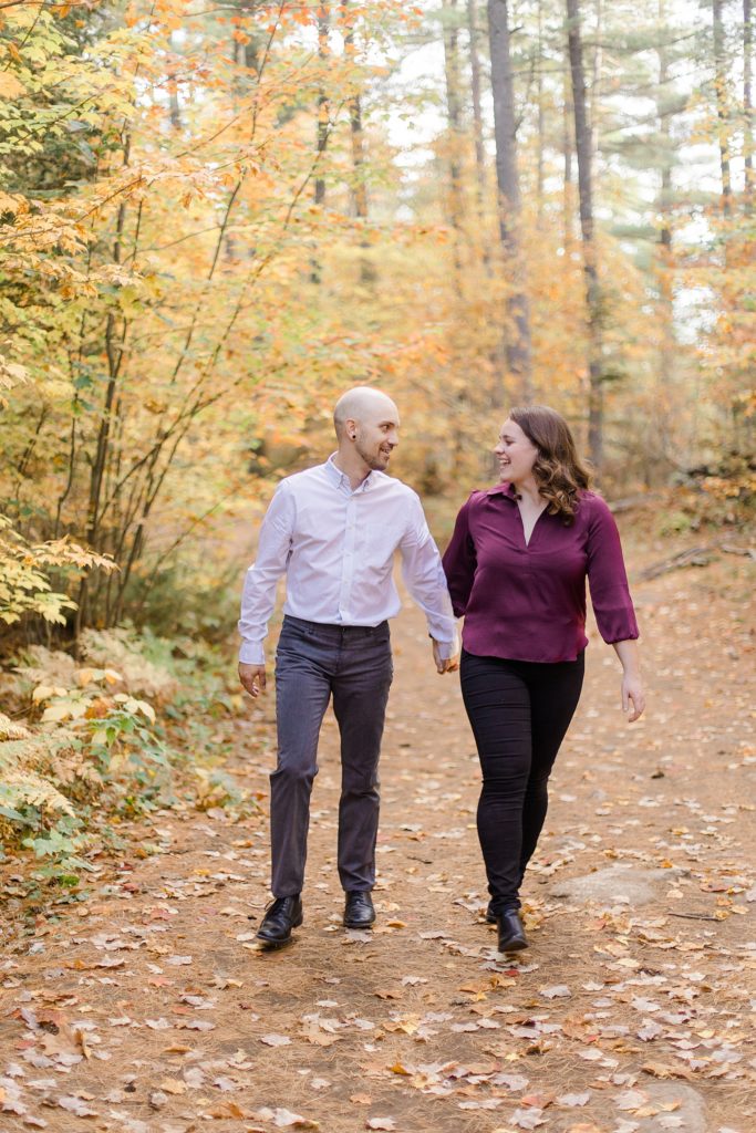 couple walking through trail filled with leaves at eagle's nest fall engagement photographed by Brittany Navin Photography