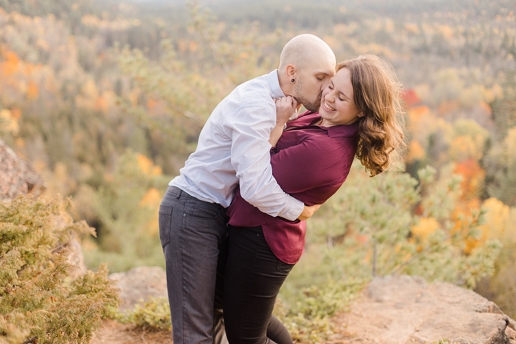 he is kissing her cheek while they stand at the top of the cliff at eagle's nest fall engagement photographed by Brittany Navin Photography