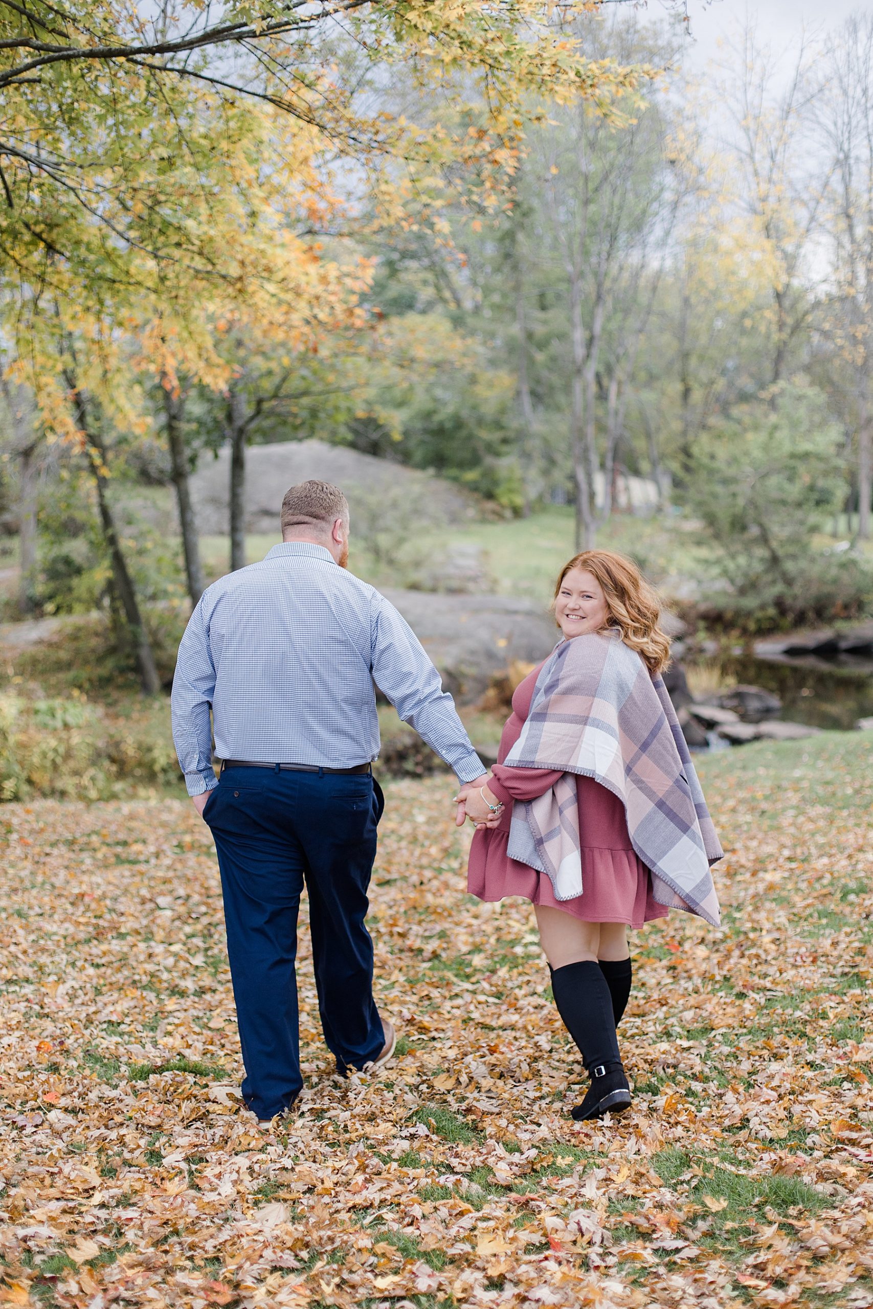 couple walking away from camera as she looks back towards the camera At Stewart Park Engagement photographed by Brittany Navin Photography