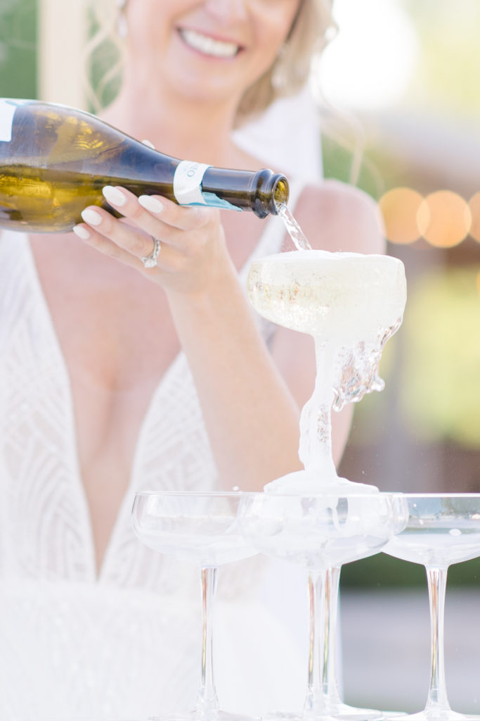 Bride pouring a champagne tower as one of the events at Stonefields wedding to ensure wedding guests have an amazing experience photographed by Brittany Navin Photography while working for Stephanie Mason and Co. 