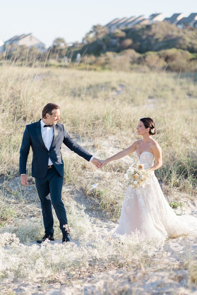 bride and groom walking through the grassy sand dunes at Omni Amelia Island Resort photographed by Brittany Navin Photography