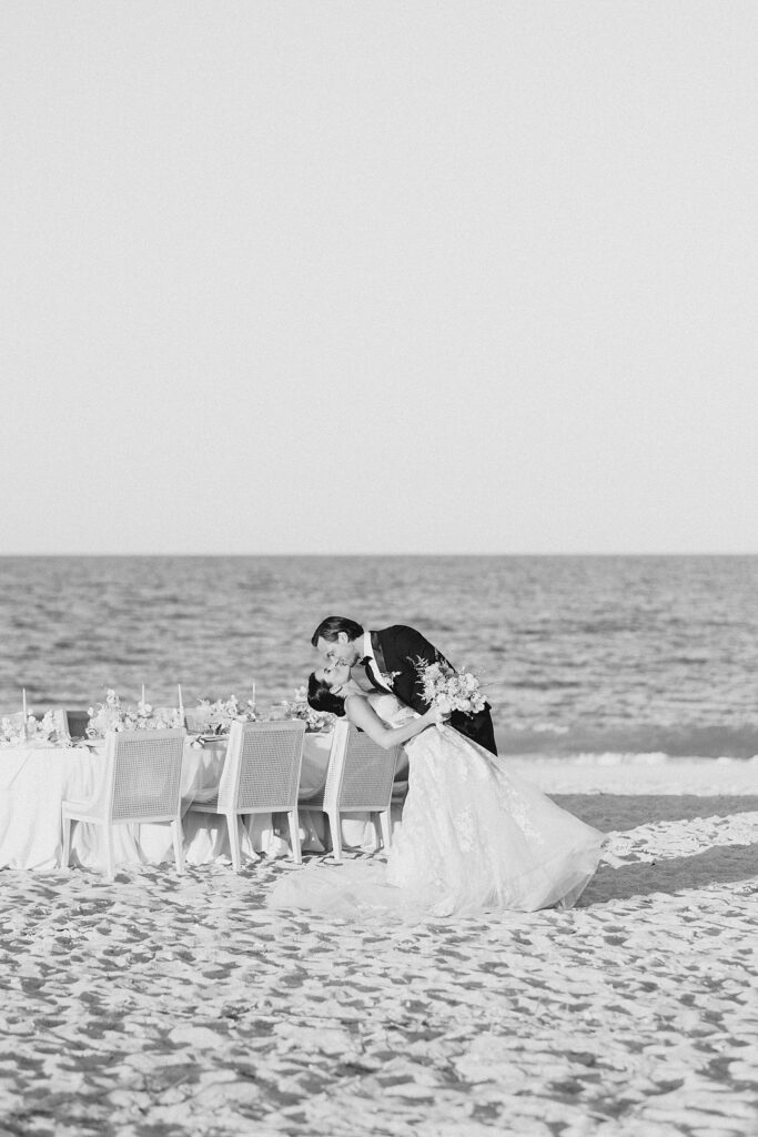 bride and groom going in for a dip kiss at their beach wedding reception at the coastal opulence beach wedding editorial photographed by Brittany Navin Photography