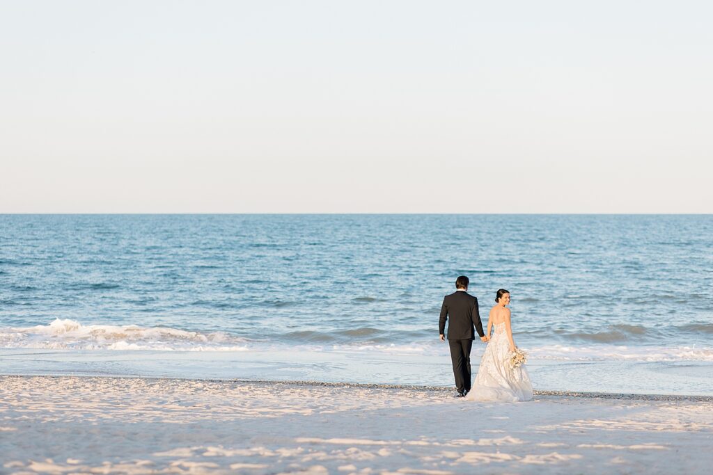 bride and groom walking towards the ocean on the beach at the coastal opulence beach wedding editorial photographed by Brittany Navin Photography