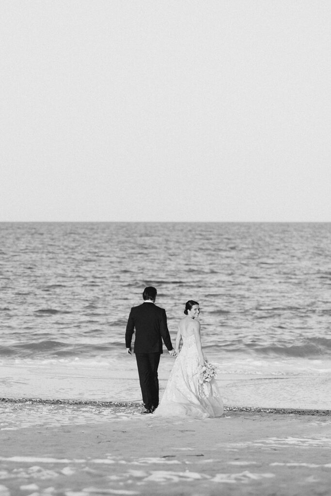 black and white image of bride and groom walking on the beach during destination wedding photographed by Brittany Navin Photography