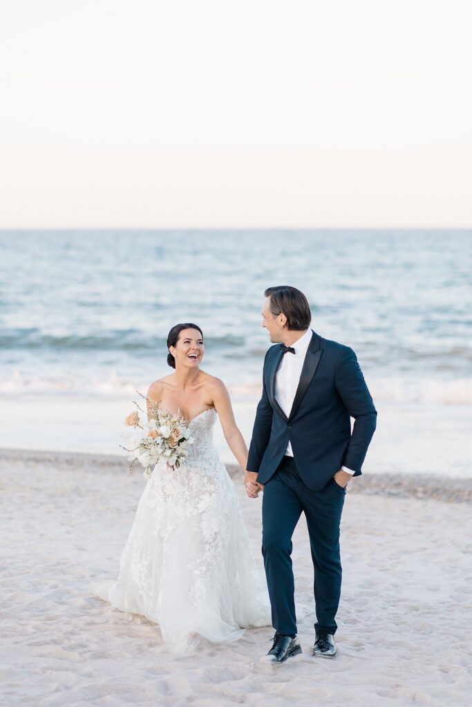 joyful bride and groom walking along the beach at the coastal opulence beach wedding editorial photographed by Brittany Navin Photography
