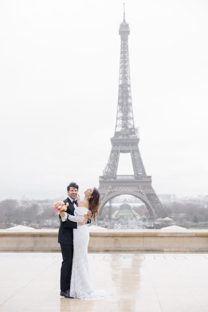 groom makes bride laugh during rainy portraits in front of the Eiffel Tower during elopement editorial in Paris, France, photographed by Brittany Navin Photography, an Ottawa based destination wedding photographer.