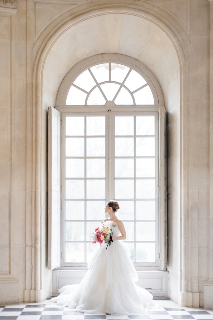 bridal portrait infront of large eauropean arched window at Chateau De Champlatreux Wedding in Paris, France photographed by destination wedding photographer Brittany Navin Photography
