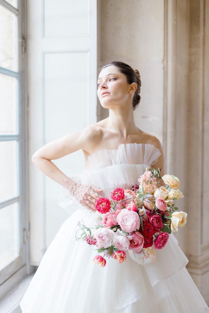 bridal portrait by window with luscious bouquet filled with pops of pink at Chateau De Champlatreux Wedding in Paris, France photographed by destination wedding photographer Brittany Navin Photography